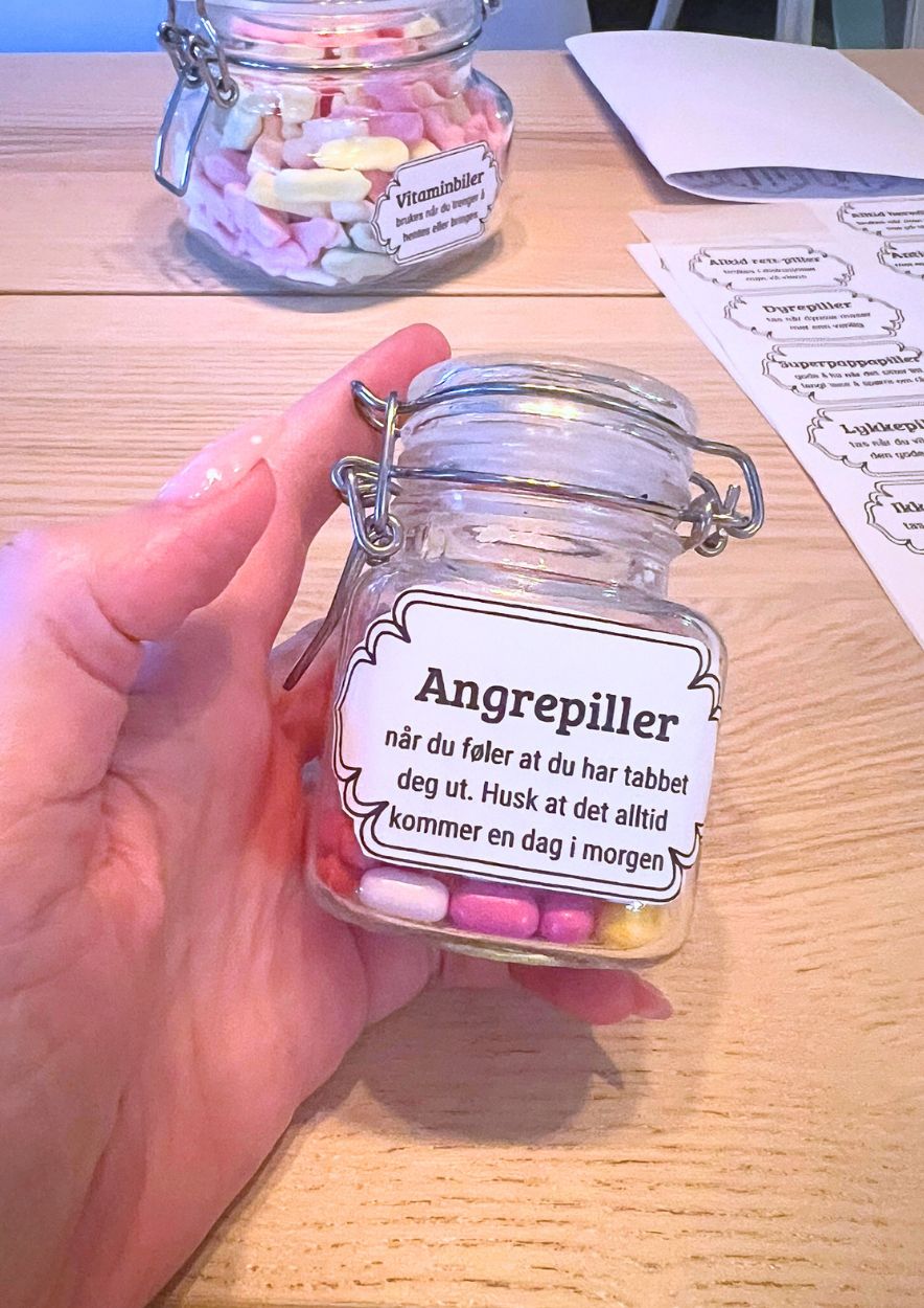 Hånd som holder en liten glasskrukke med rødt godteri og vintageetiketten «Angrepiller»