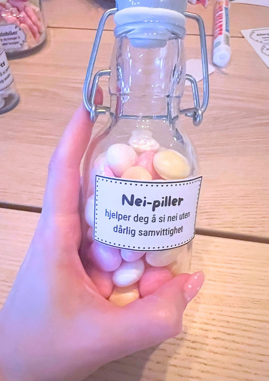 Hånd som holder en glasskrukke med pastellgodteri og den prikkede etiketten «Nei-piller»