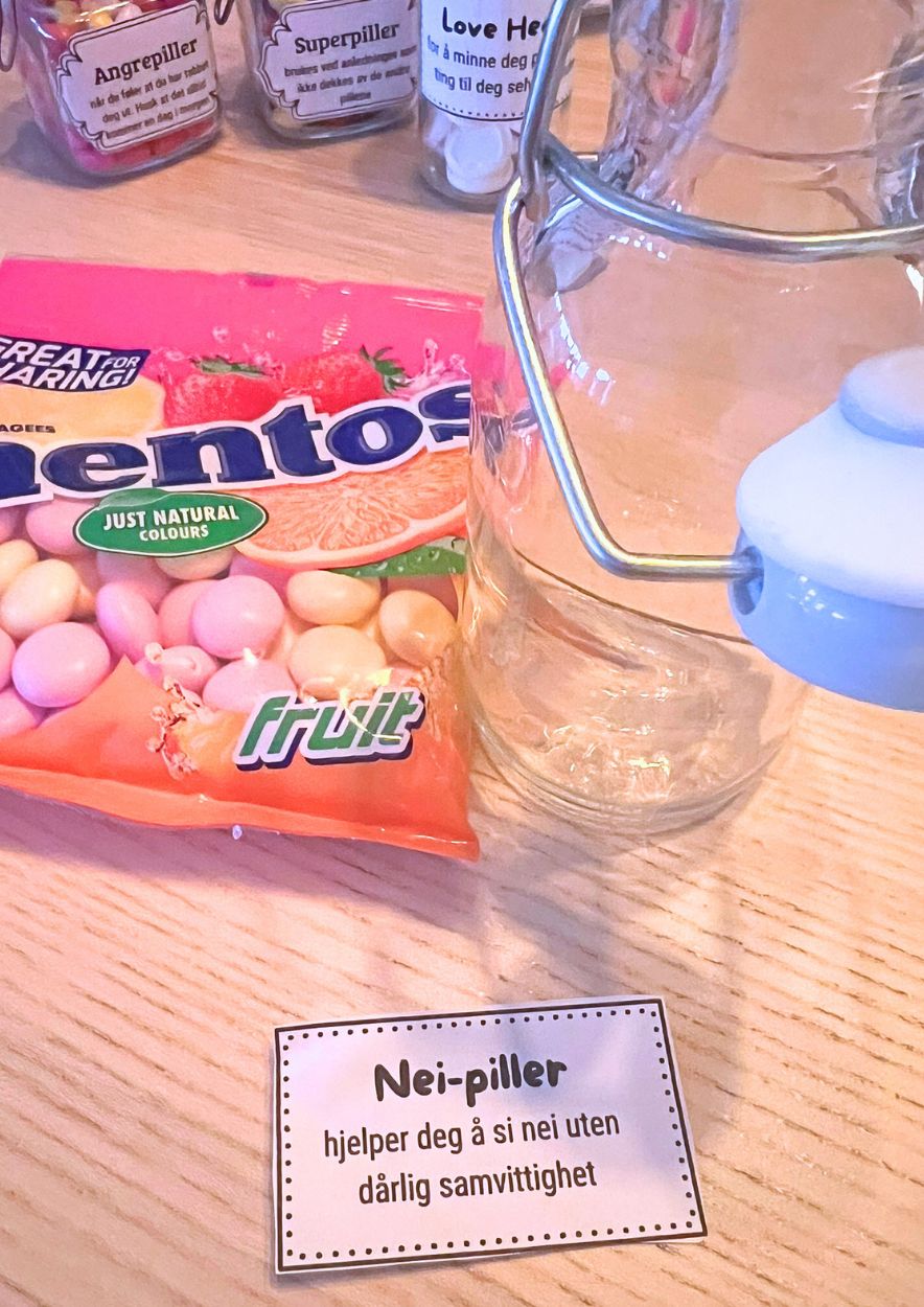 Frukt-Mentos, tomme glasskrukker og en utskrevet «Nei-piller»-etikett på et lyst trebord
