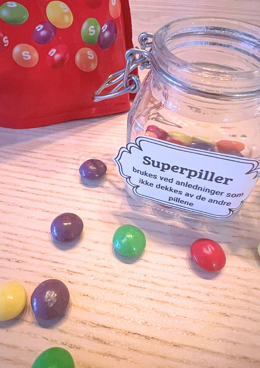 Liten glasskrukke med fargerikt godteri (Skittles) og vintageetiketten «Superpiller»