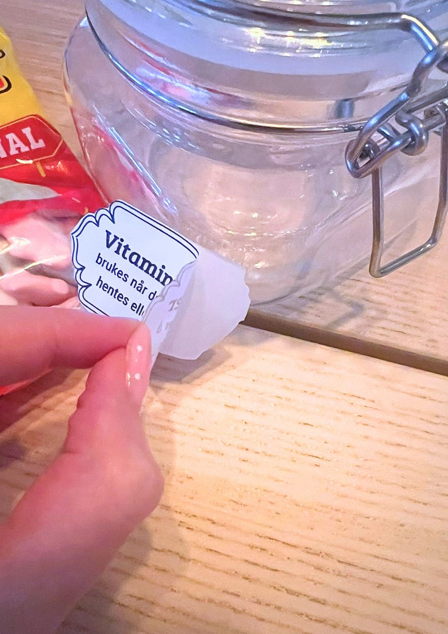 Hånd som fester «Vitaminbiler»-etiketten på en tom glasskrukke