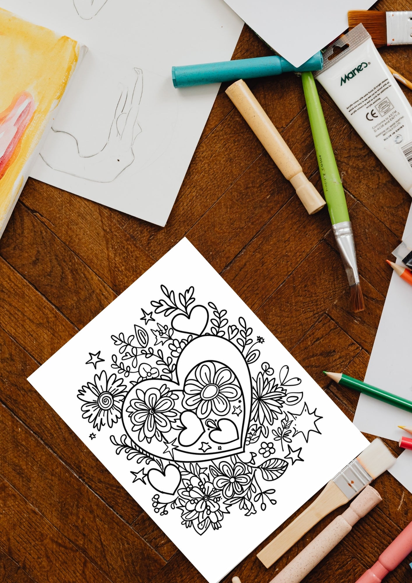 Fargeleggingsside med et stort hjerte fylt med blomster og blader, omgitt av mindre hjerter og dekorative elementer – vist med fargeblyanter og pensler