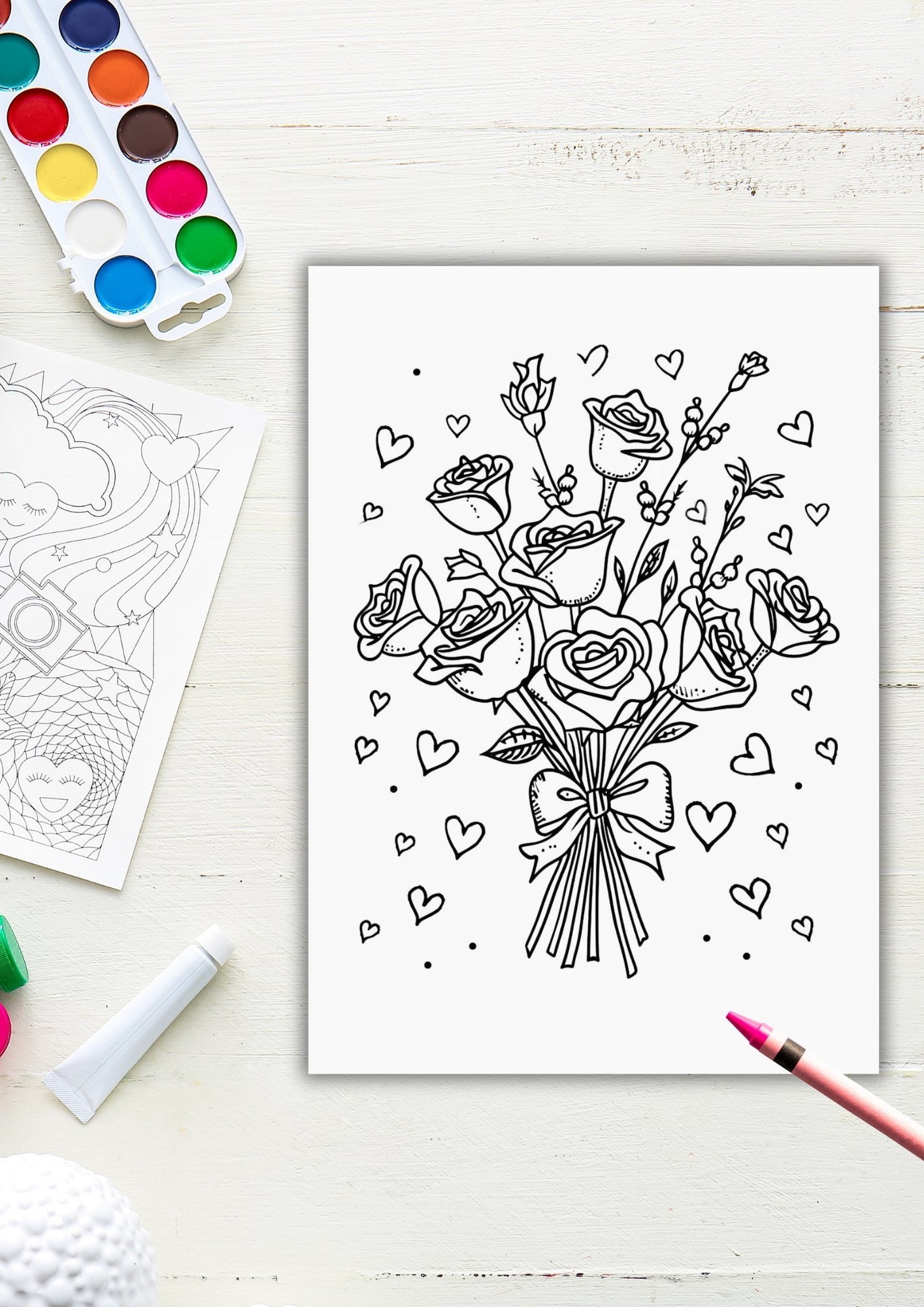 Fargeleggingsside med en rosebukett bundet med sløyfe, omgitt av mange små hjerter – vist med vannfarger og fargestifter på hvitt bord